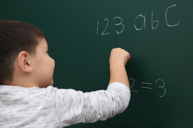 Photo of Little child writing math sum on chalkboard