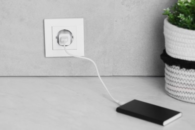 Photo of Power bank plugged into electric socket on white table