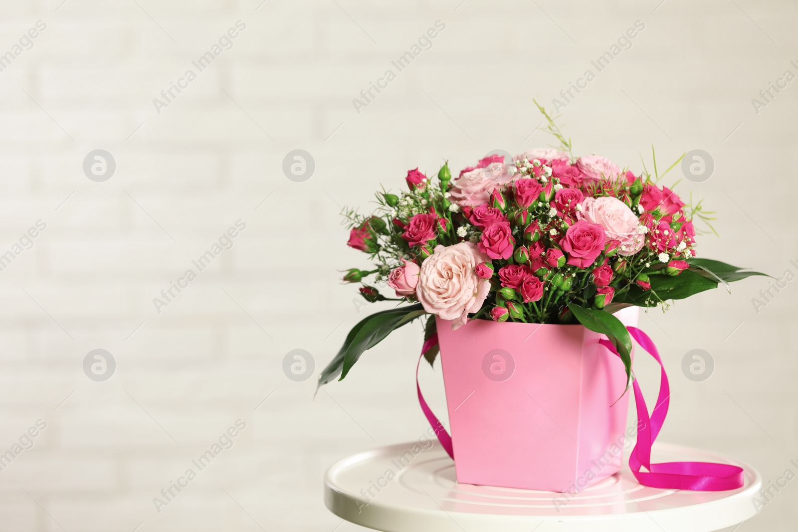 Photo of Beautiful bouquet of flowers in paper gift box on table against light background. Space for text