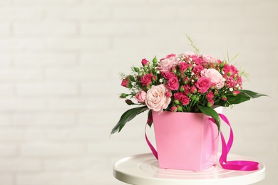 Beautiful bouquet of flowers in paper gift box on table against light background. Space for text