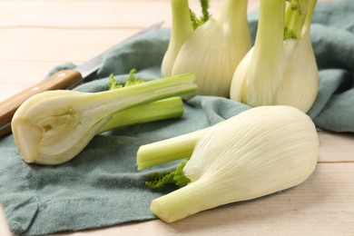 Photo of Fresh raw fennel bulbs and knife on light wooden table, closeup