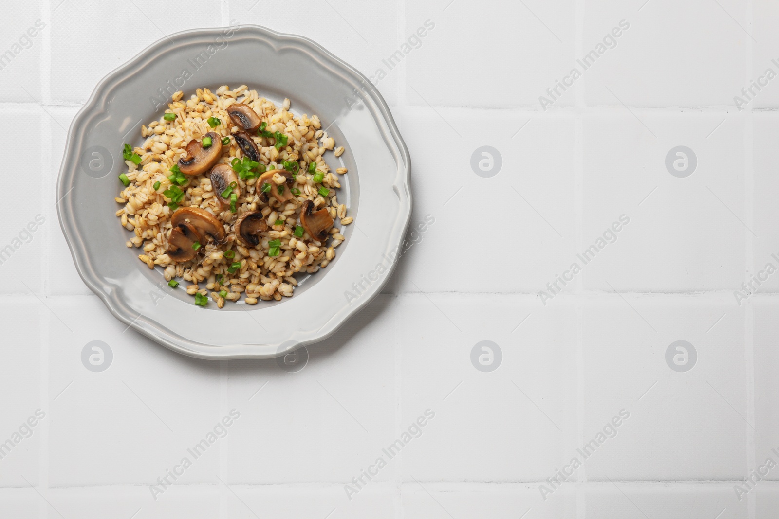 Photo of Delicious pearl barley with onion and mushrooms on white tiled table, top view. Space for text