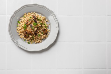 Delicious pearl barley with onion and mushrooms on white tiled table, top view. Space for text