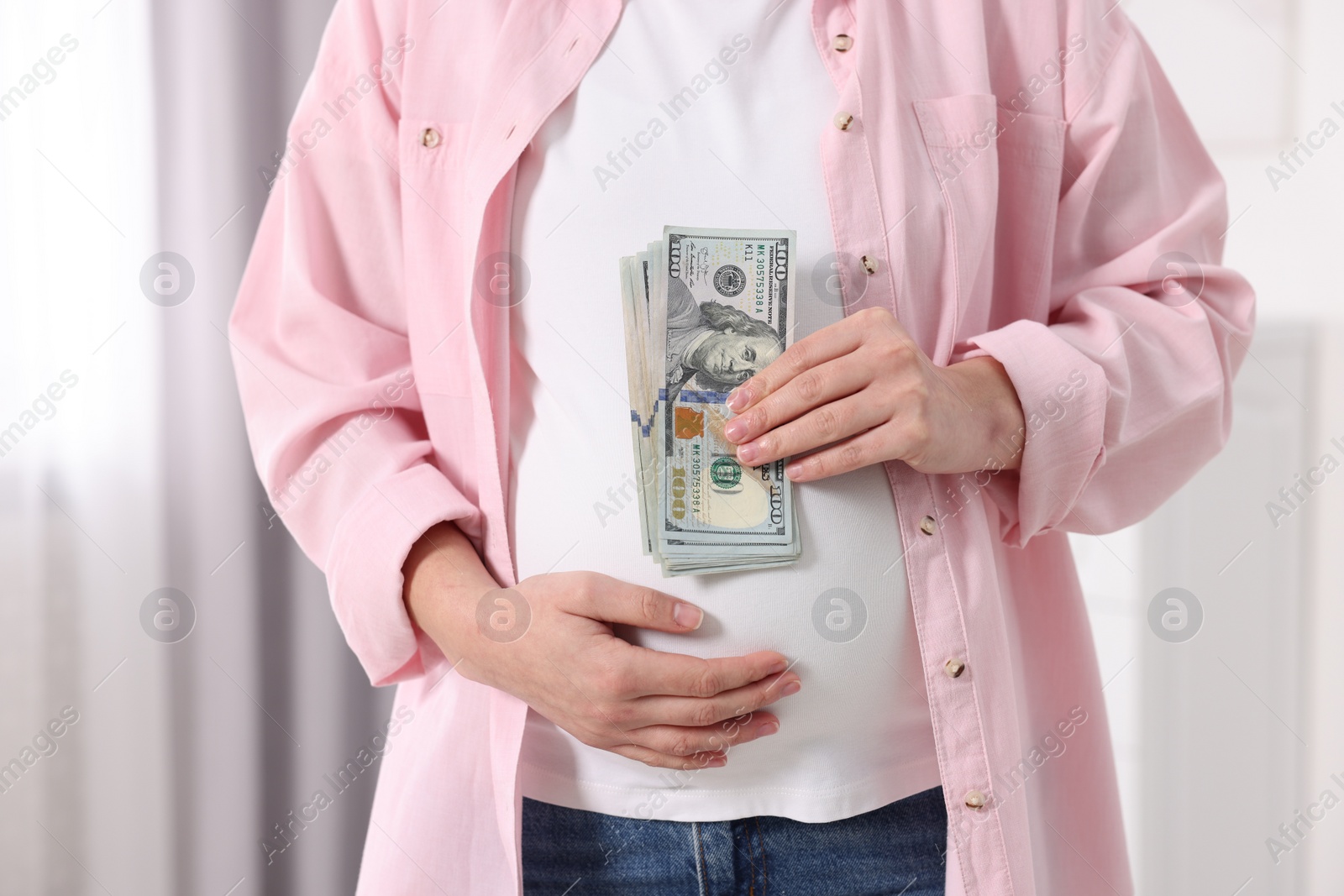 Photo of Surrogate mother. Pregnant woman with dollar banknotes indoors, closeup