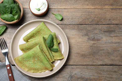 Photo of Delicious spinach crepes served on wooden table, flat lay. Space for text