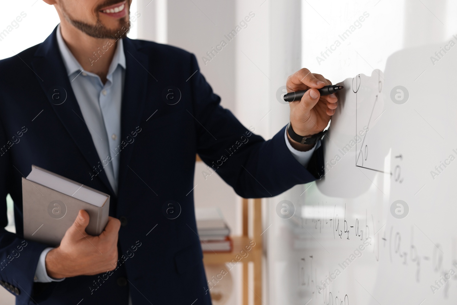 Photo of Happy teacher with book explaining mathematics at whiteboard in classroom, closeup