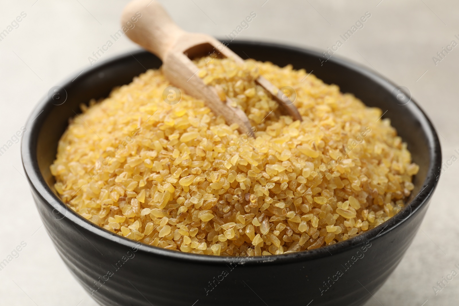 Photo of Bowl and scoop with raw bulgur on gray background, closeup
