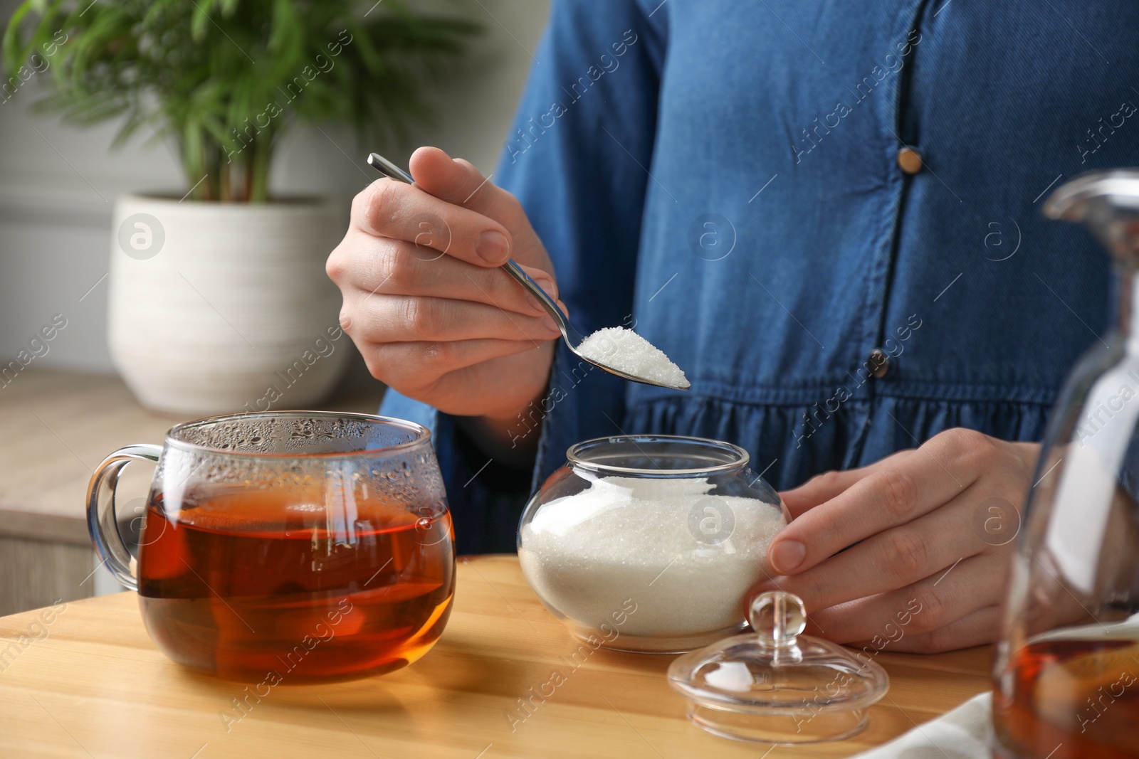 Photo of Woman adding sugar into aromatic tea at wooden table indoors, closeup