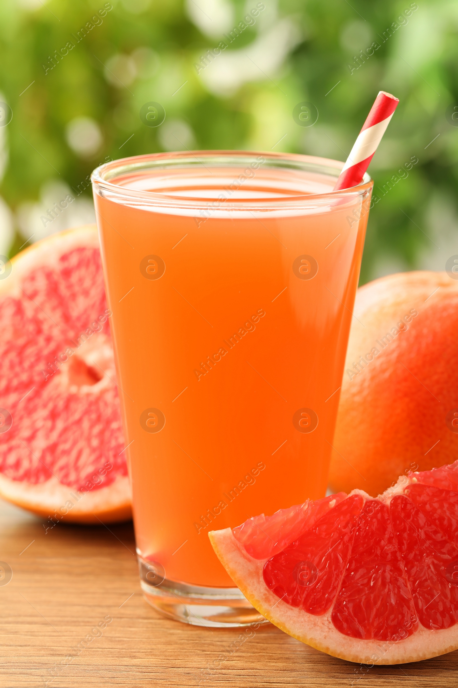 Photo of Glass of delicious grapefruit juice on wooden table against blurred background