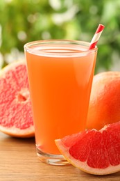 Photo of Glass of delicious grapefruit juice on wooden table against blurred background