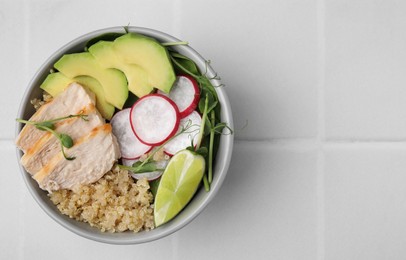Photo of Delicious quinoa salad with chicken, avocado and radish on white tiled table, top view. Space for text