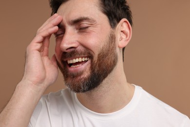 Photo of Handsome man laughing on light brown background, closeup