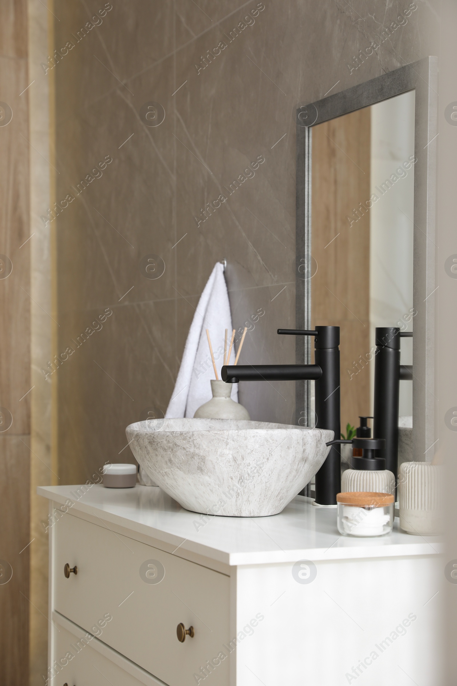 Photo of Stone vessel sink with faucet and toiletries on white countertop in bathroom