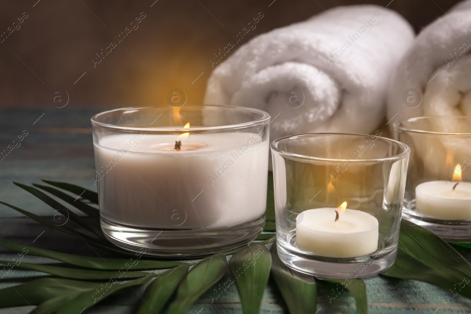 Photo of Spa composition with burning wax candles, towels and tropical leaf on table