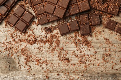 Photo of Pieces and shavings of tasty chocolate bars on wooden table, flat lay. Space for text