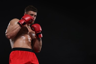 Photo of Man in boxing gloves fighting on black background. Space for text