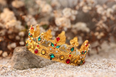 Photo of Beautiful golden crown on sand outdoors, closeup. Fantasy item