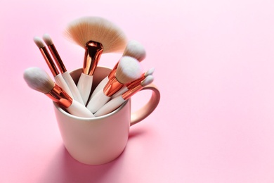 Photo of Professional makeup brushes in cup on pink background. Space for text