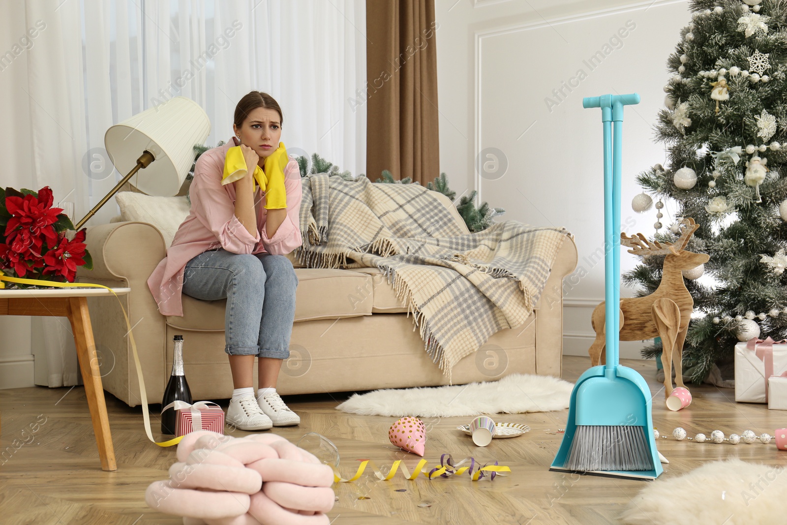 Photo of Tired woman sitting in messy room while cleaning after New Year party