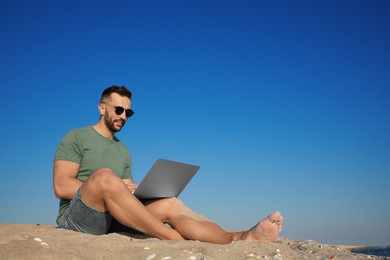 Photo of Man working with laptop on beach. Space for text