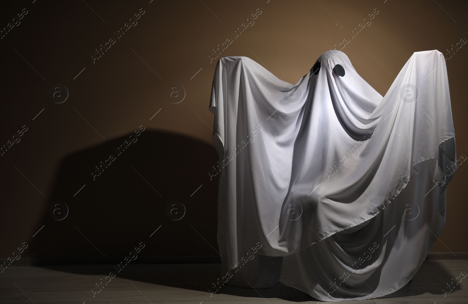 Photo of Creepy ghost. Woman covered with sheet near brown wall, space for text