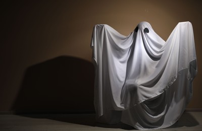 Creepy ghost. Woman covered with sheet near brown wall, space for text
