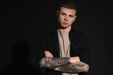 Photo of Young man with tattoos on black background. Space for text