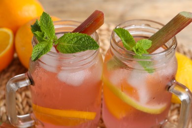 Photo of Mason jars of tasty rhubarb cocktail with citrus fruits on table, closeup