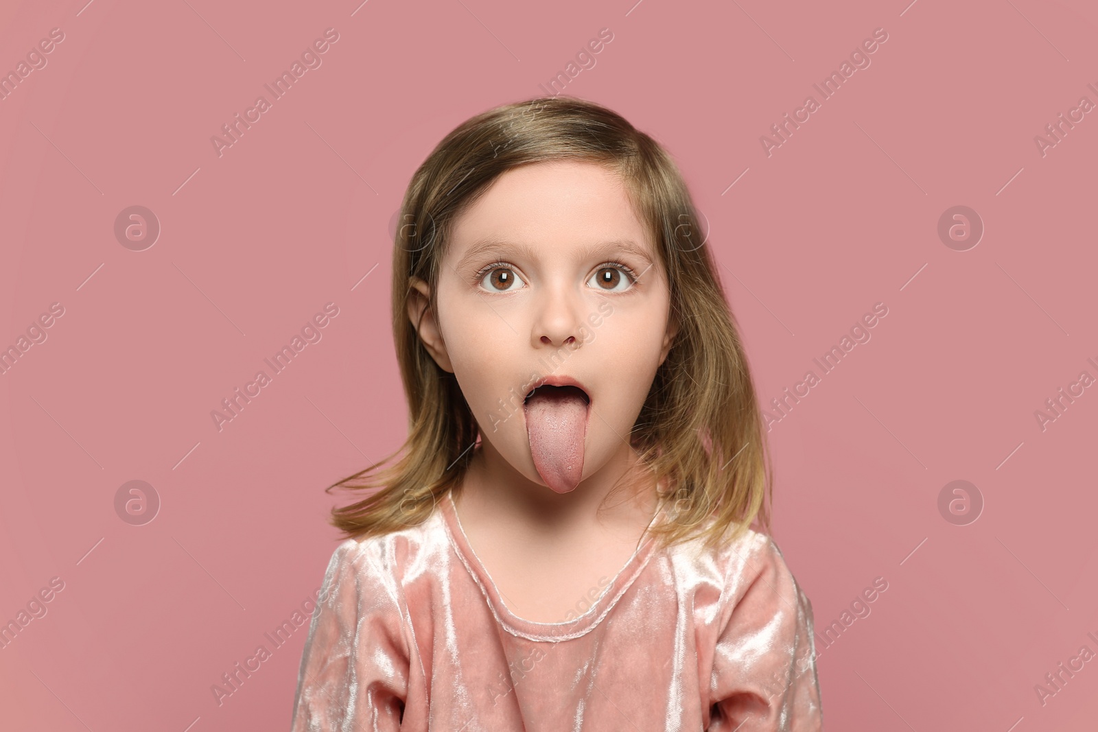 Photo of Funny little girl showing her tongue on pink background