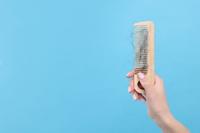 Woman holding comb with lost hair on light blue background, closeup and space for text. Alopecia problem