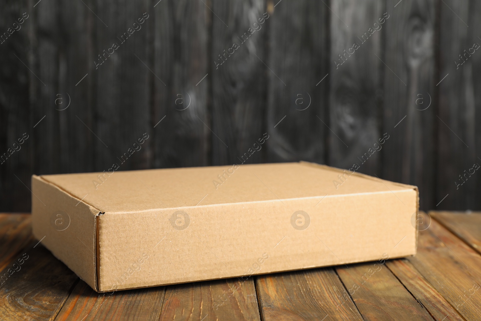 Photo of Cardboard box on wooden table against dark background