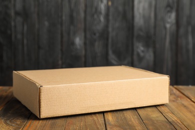 Photo of Cardboard box on wooden table against dark background