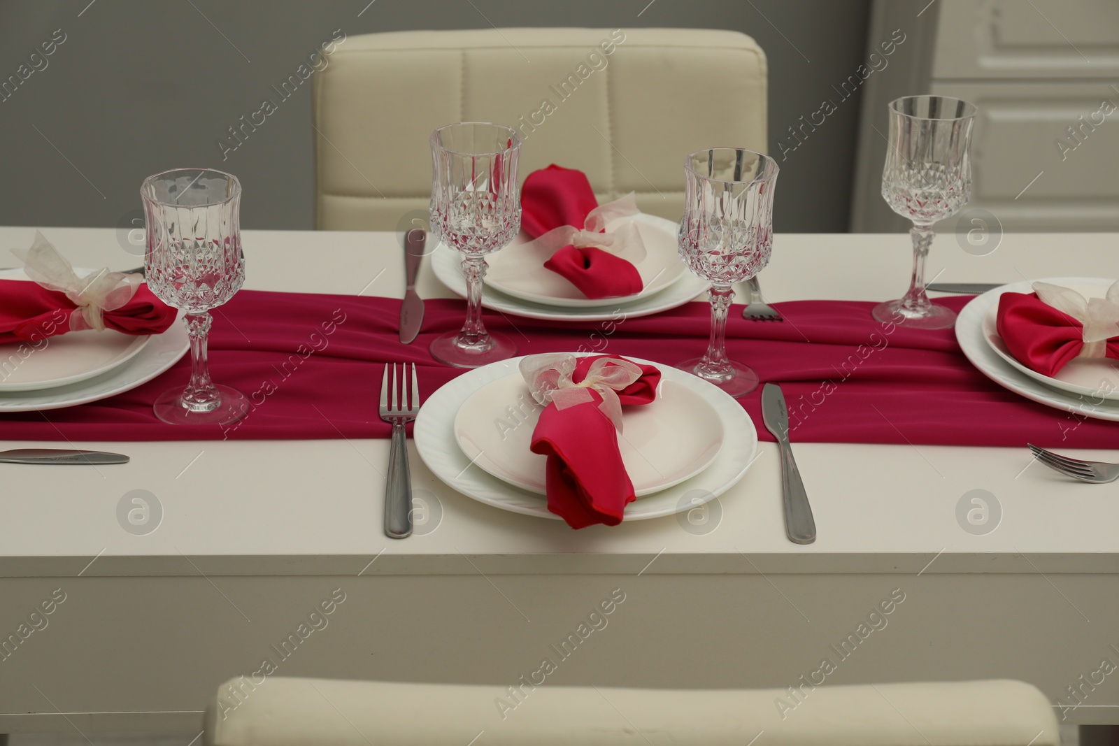 Photo of Color accent table setting. Glasses, plates, cutlery and pink napkins in dining room