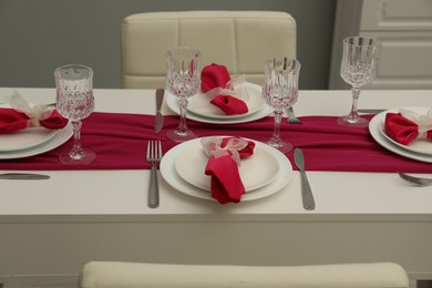 Color accent table setting. Glasses, plates, cutlery and pink napkins in dining room