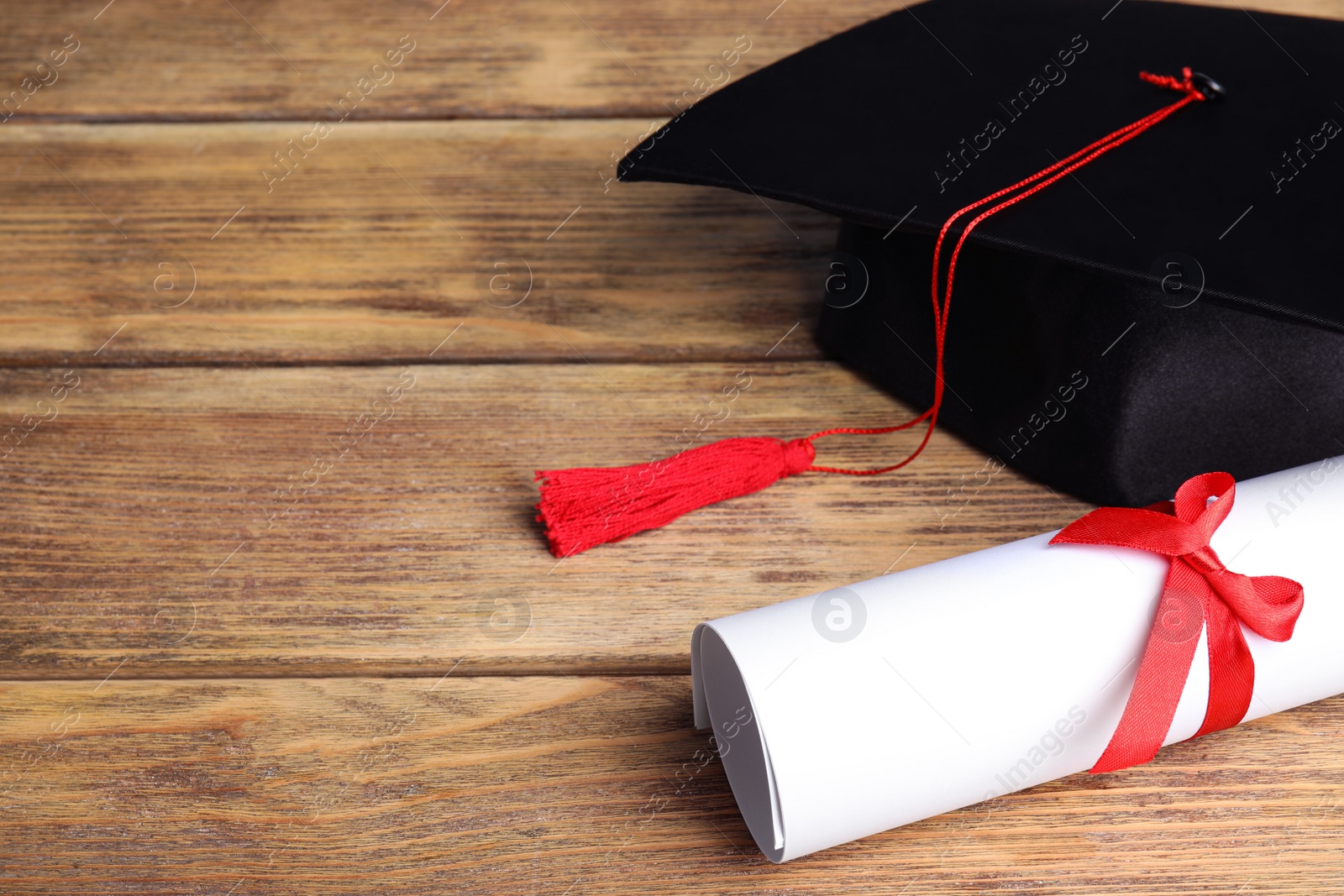 Photo of Graduation hat and student's diploma on wooden table, space for text