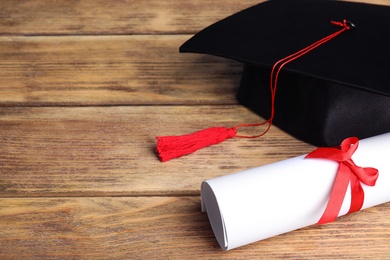 Graduation hat and student's diploma on wooden table, space for text