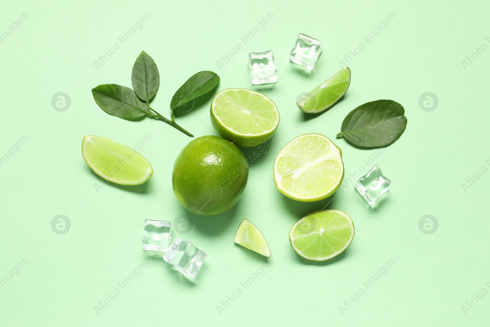 Photo of Fresh ripe limes with leaves and ice cubes on light green background, flat lay