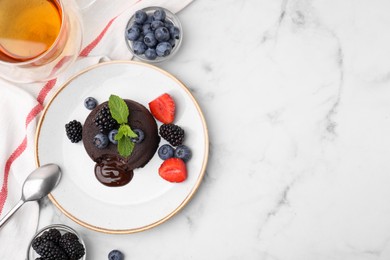 Plate with delicious chocolate fondant, berries and mint on white marble table, flat lay. Space for text