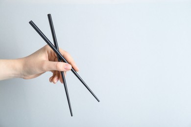 Woman holding pair of black chopsticks on light grey background, closeup. Space for text