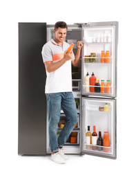 Photo of Man with bottle of juice near open refrigerator on white background