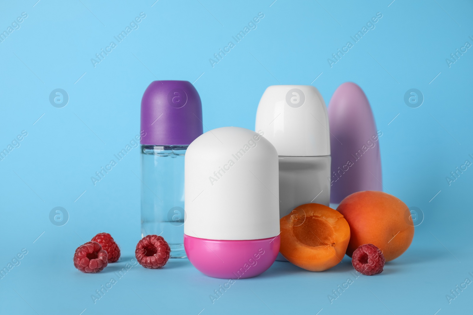 Photo of Different female roll-on deodorants, apricots and raspberries on light blue background