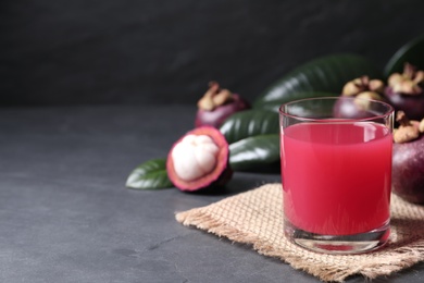 Photo of Delicious fresh mangosteen juice in glass on dark table, space for text