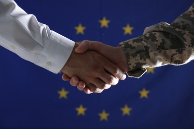 Photo of Soldier and businessman shaking hands against flag of European Union, closeup