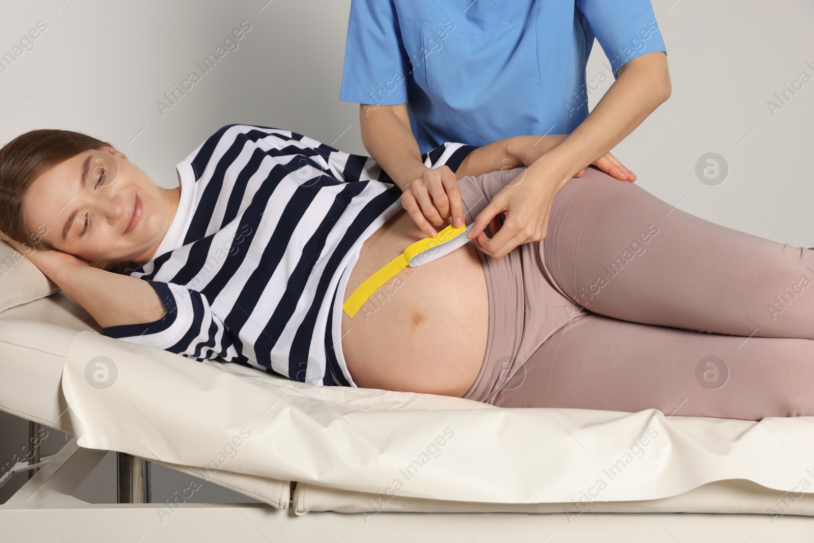 Photo of Pregnant woman visiting physiotherapist. Doctor applying kinesio tape indoors, closeup