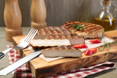 Photo of Cut grilled pork steaks and cutlery on table, closeup