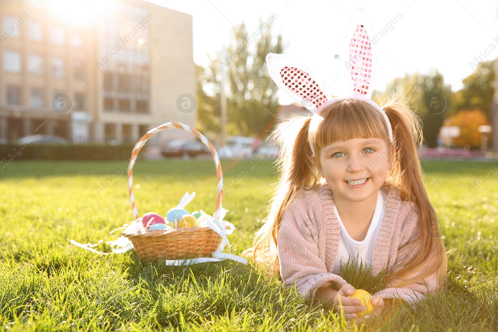 Photo of Cute little girl with bunny ears and basket of Easter eggs in park