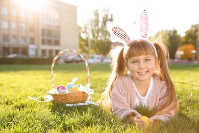 Cute little girl with bunny ears and basket of Easter eggs in park