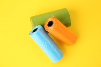 Photo of Colorful dog waste bags on yellow background, above view