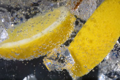 Juicy lemon slices and ice cubes in soda water against black background, closeup