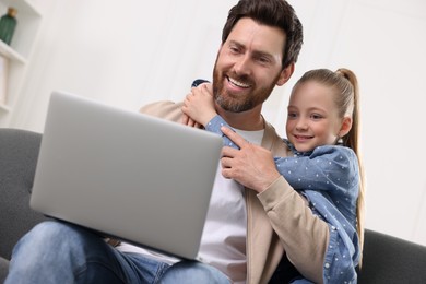 Happy man and his daughter with laptop on sofa at home